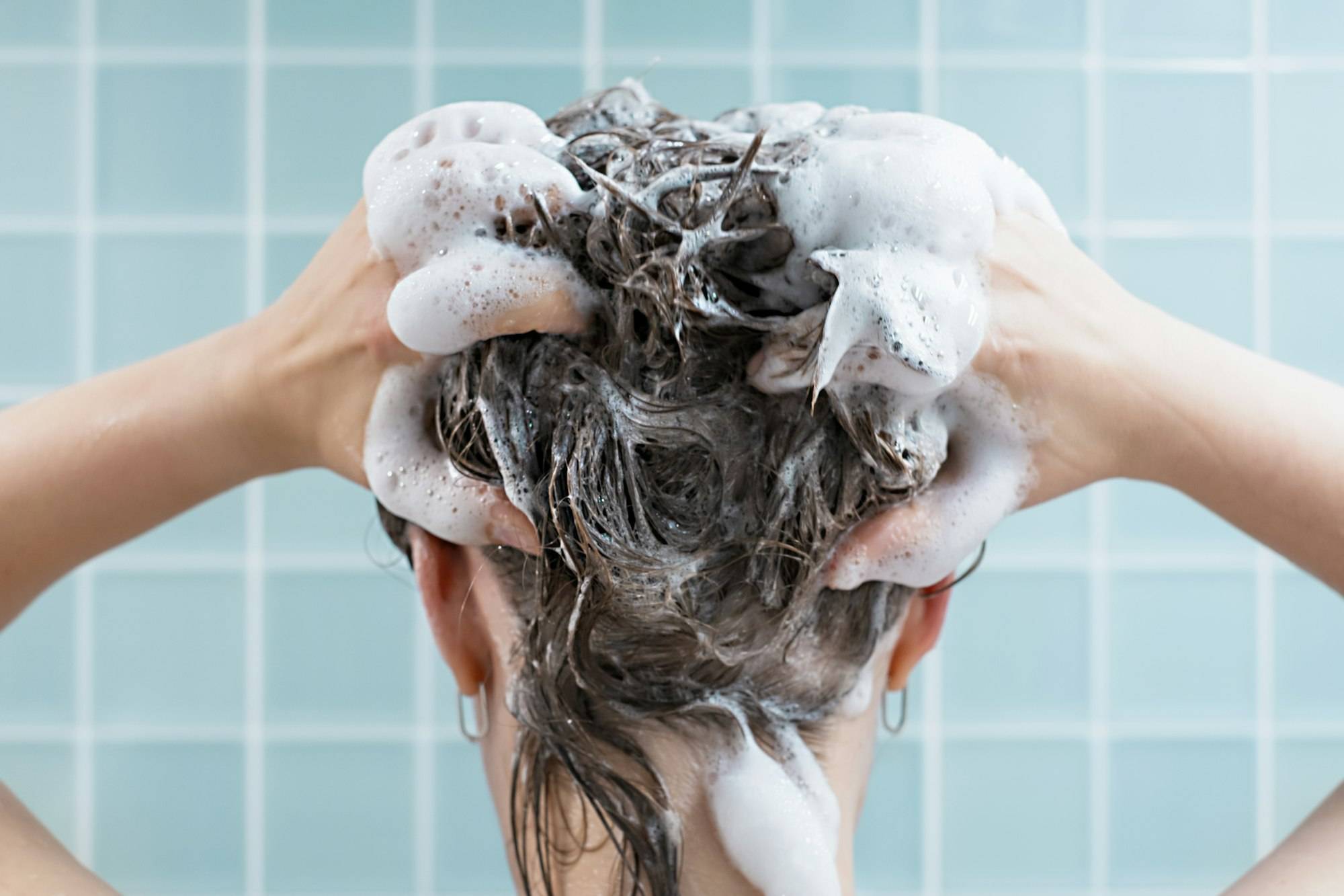 Girl washes her hair with shampoo on blue background, back view